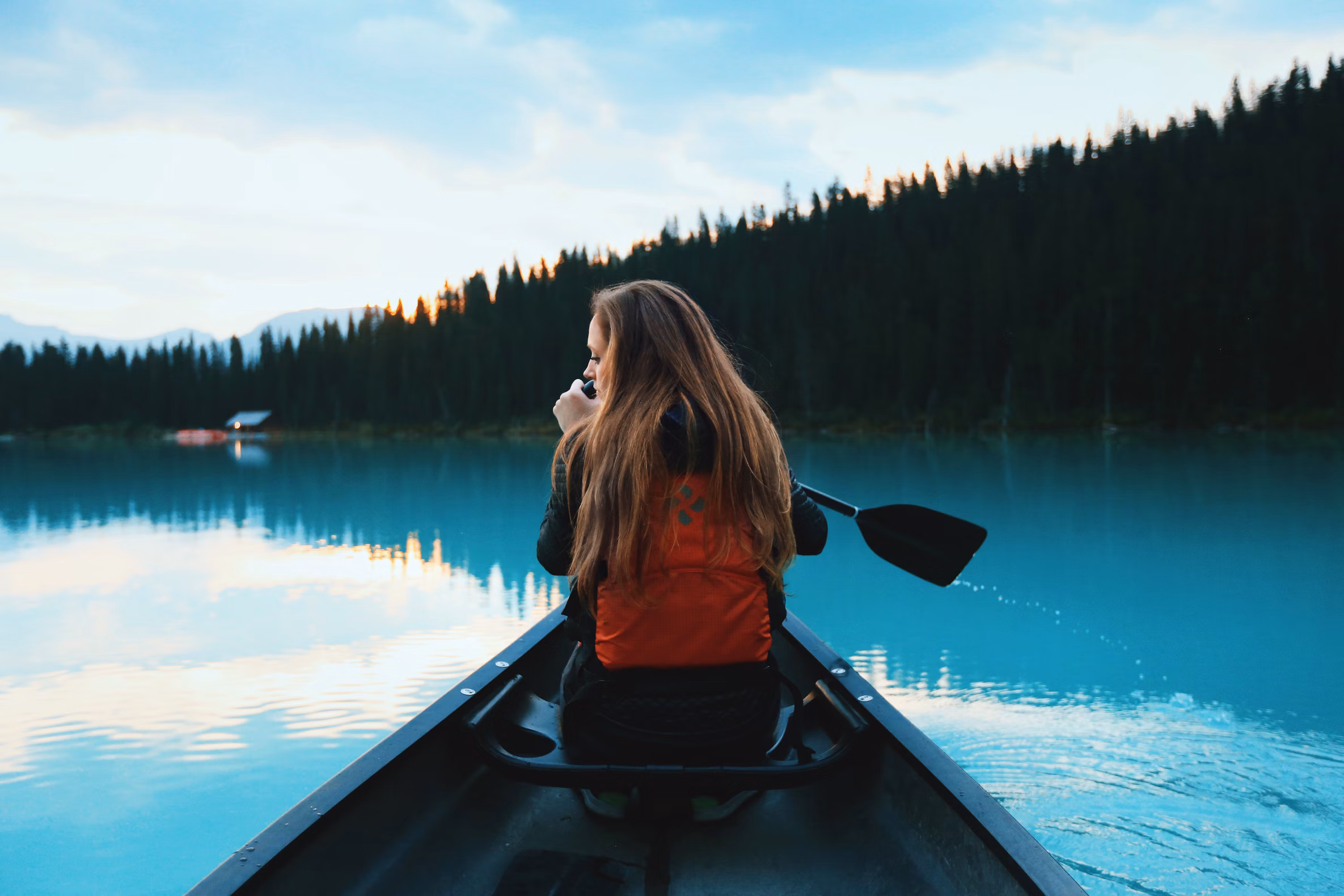Woman paddling a canoe on a calm blue lake surrounded by forest