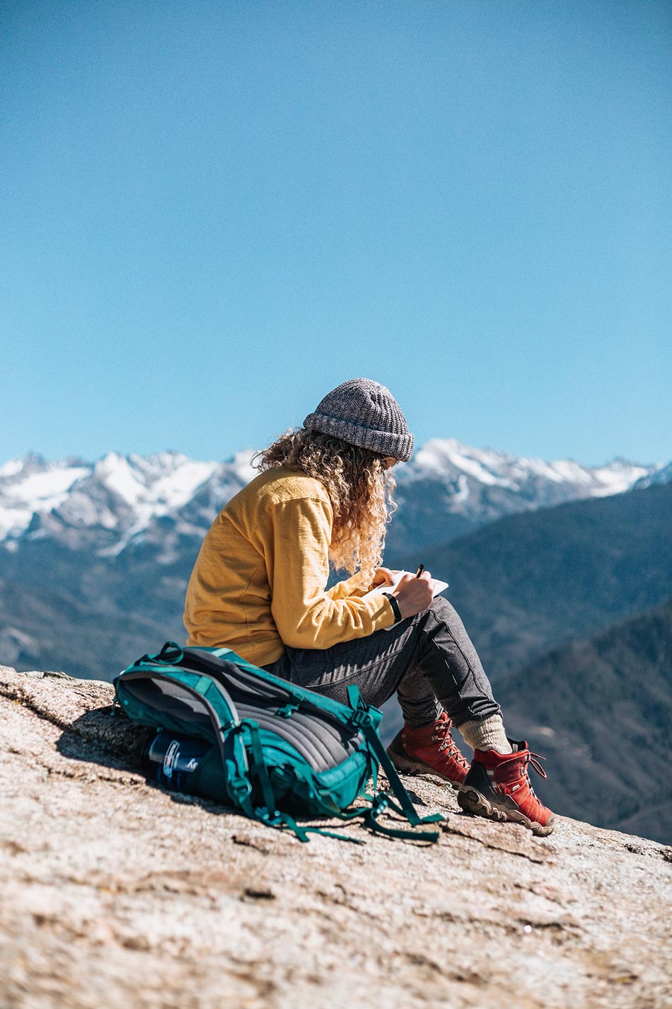 woman writing while sitting on hill with mountain background